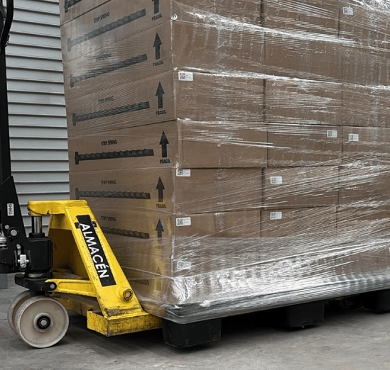 A yellow pallet jack moving a shrink-wrapped pallet inside a warehouse.
