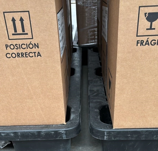 Two cardboard boxes labeled in Spanish on a black plastic pallet.